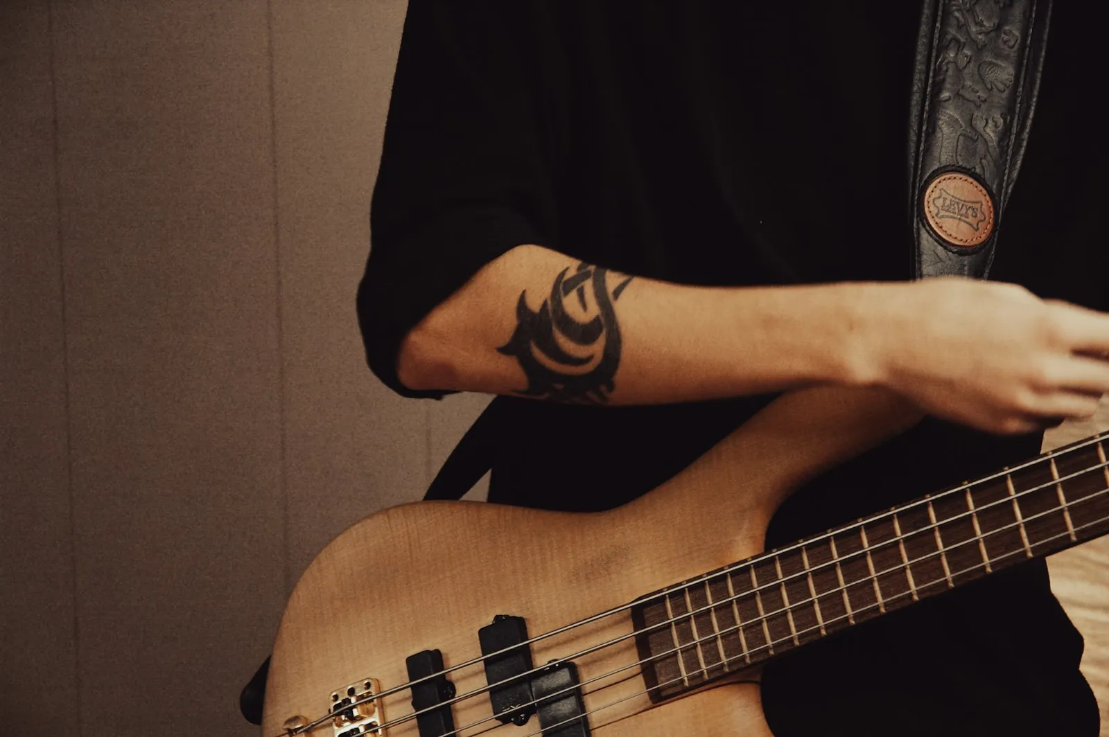 Detail muzikanta hrajícího na baskytaru z přírodního dřeva
